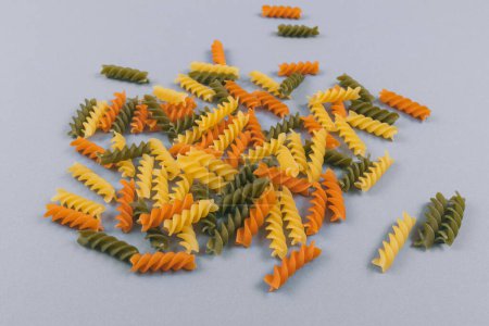 Set of scattered three-colored pasta on gray background. 