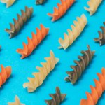 Lines made of three-colored Fusilli pasta on blue background. Close-up. Macro photo. Concept. Food pattern.