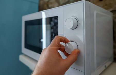 Foto de El hombre utiliza un horno microondas en la cocina. - Imagen libre de derechos