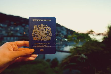 Woman holding UK passport against the backdrop of a tropical country.
