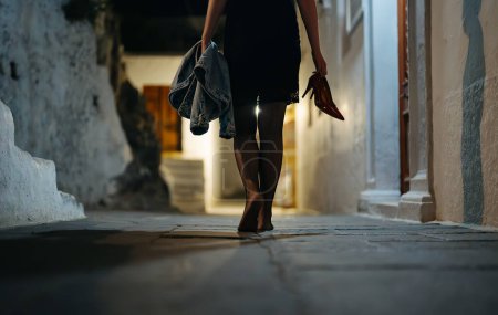 Woman walks home barefoot at night after a party.