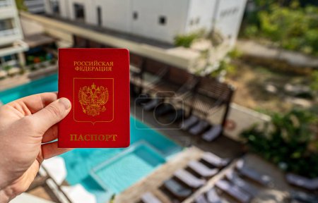 Téléchargez les photos : Homme tenant un passeport russe dans le contexte d'un hôtel de luxe. - en image libre de droit