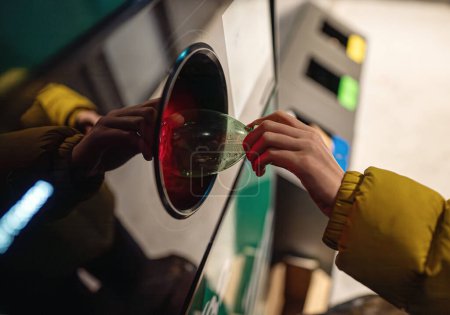 Woman puts bottle in automatic bottle recycling machine. Reverse vending recycling machine.