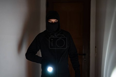 Cambrioleur masqué avec lampe torche vérifier appartement.