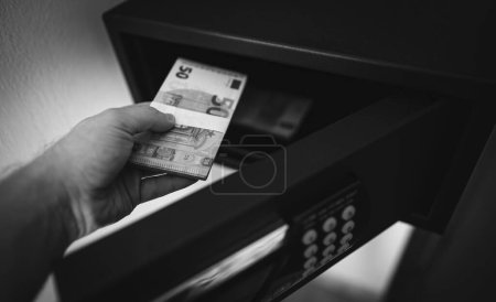 El hombre pone o toma billetes en euros de una caja fuerte.