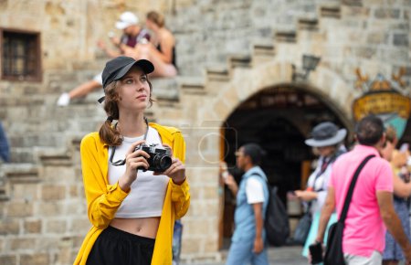 Fille avec un appareil photo vintage sur la place parmi les touristes.