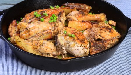 Téléchargez les photos : Poulet au four Vésuve servi dans une poêle en fonte servi avec des pommes de terre rôties et des pois dans une sauce à l'ail et au citron. - en image libre de droit