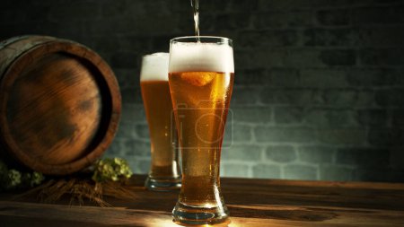 Téléchargez les photos : Glass of light beer pouring on wooden table. Still life shot with wooden keg on background. - en image libre de droit