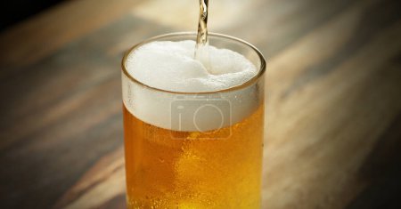 Foto de Glass of light beer pouring on wooden table. Studio shot with isolated glass of beer. - Imagen libre de derechos