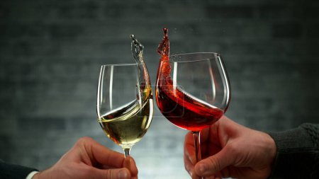 Foto de Two men clinking with glasses of wine, celebrating success or speaking toast, close-up. Wine is splashing out of glasses. - Imagen libre de derechos