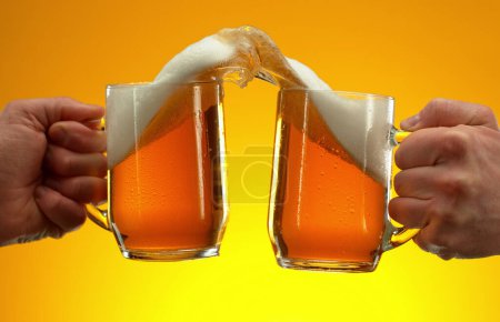 Photo for Two glasses of beer in cheers gesture, splashing out. Isolated on golden background. - Royalty Free Image