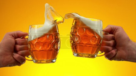 Téléchargez les photos : Two glasses of beer in cheers gesture, splashing out. Isolated on golden background. - en image libre de droit