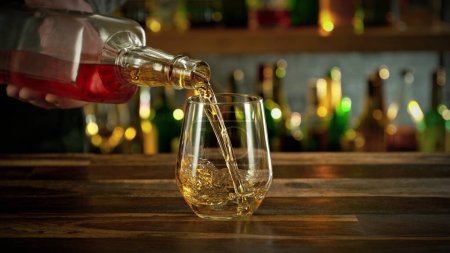 Foto de Ice cube fall into a glass with a golden alcoholic drink. Bar on background. - Imagen libre de derechos