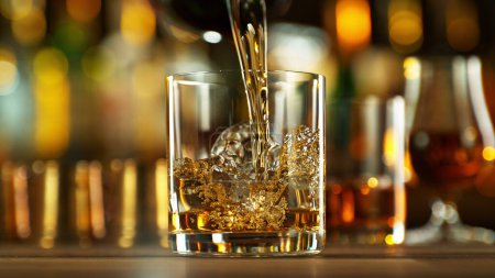 Téléchargez les photos : Ice cube fall into a glass with a golden alcoholic drink. Bar on background. - en image libre de droit