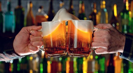 Téléchargez les photos : Close-up view of a two glasses of beer in hands. Beer glasses clinking at bar or pub. - en image libre de droit