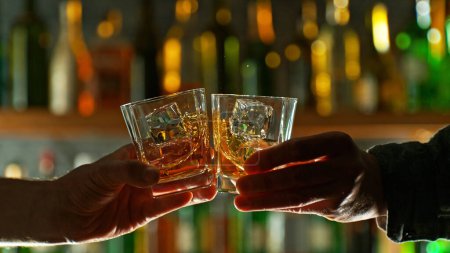 Photo for Close-up view of a two whiskey shots in hands. Glasses clinking at bar or pub - Royalty Free Image