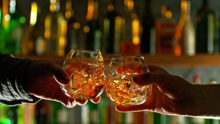 Téléchargez les photos : Close-up view of a two whiskey shots in hands. Glasses clinking at bar or pub - en image libre de droit