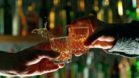 Téléchargez les photos : Close-up view of a two hard liquor shots in hands. Glasses clinking at bar or pub - en image libre de droit