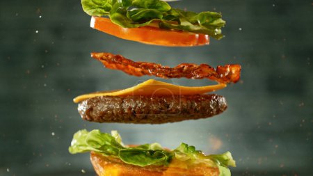 Foto de Hamburguesa de queso con ingredientes voladores, movimiento de congelación realista, fondo de pared gris oscuro. - Imagen libre de derechos