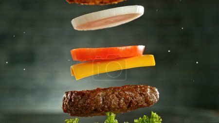 Téléchargez les photos : Cheeseburger aux ingrédients volants, mouvement de gel réaliste, fond mural gris foncé. - en image libre de droit