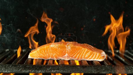 Téléchargez les photos : Barbecue grill avec steak de saumon cru. Barbecue grille de feu sur fond noir. - en image libre de droit