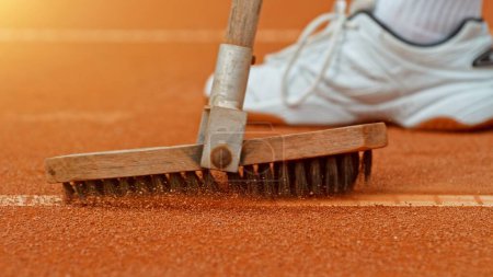 Téléchargez les photos : Joueur de tennis nettoie une ligne de court de tennis avec une brosse. Détail de la chaussure et de la brosse sur surface argileuse. - en image libre de droit