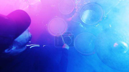 Photo for Drummer Playing on Drums Assembly. Dramatic Scene with Colored Neon Lights. Concert and Performance Theme. - Royalty Free Image
