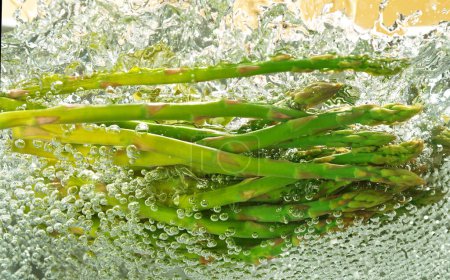 Téléchargez les photos : Prise de vue au gel des éclaboussures d'asperges fraîches. Chute de légumes dans de l'eau bouillante. Tourné dans un pot en acier. - en image libre de droit