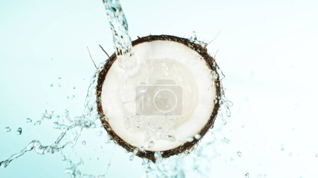 Téléchargez les photos : Noix de coco fissurée avec éclaboussures d'eau sur fond bleu. Arrêt du tournage studio, détail. - en image libre de droit