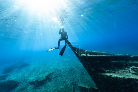 Photo for Freediver Sitting at Shipwreck Under the Sea Level and Showing OK Symbol. Young Man Diver Eploring Sea Life. - Royalty Free Image