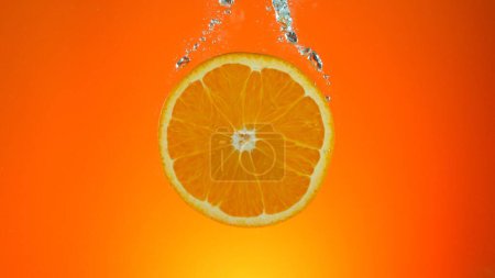 Téléchargez les photos : Tranche d'orange fraîche sous l'eau, isolée sur fond coloré. - en image libre de droit