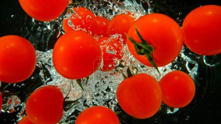 Foto de Tomates Cherry Enteros Caídos en Agua. Con burbujas de aire y salpicaduras aisladas sobre fondo negro. - Imagen libre de derechos