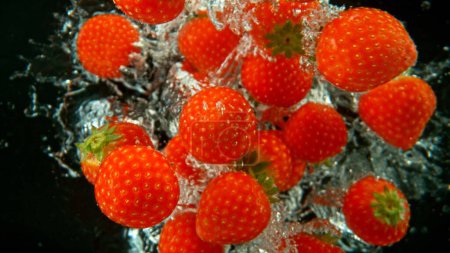 Téléchargez les photos : Des fraises fraîches tombées dans l'eau. Avec bulles d'air et éclaboussures isolées sur fond noir. - en image libre de droit