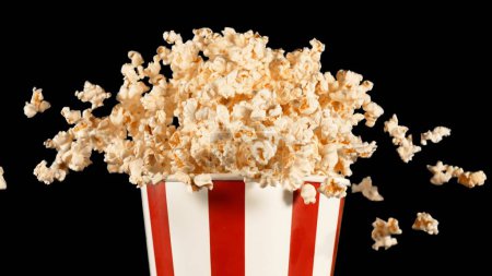 Téléchargez les photos : Popcorn Voler dans les airs depuis Paper Bucket. Isolé sur fond noir. - en image libre de droit