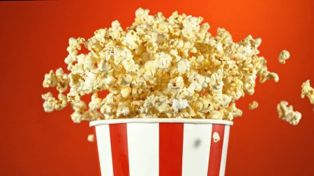 Téléchargez les photos : Popcorn Voler dans les airs depuis Paper Bucket. Isolé sur fond rouge. - en image libre de droit