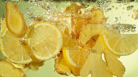 Téléchargez les photos : Congeler le mouvement des tranches de gingembre et de citron tombant dans l'eau. Épice fraîche dans l'eau. - en image libre de droit