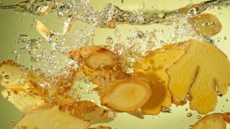 Téléchargez les photos : Congeler le mouvement des tranches de gingembre tombant dans l'eau. Épice fraîche dans l'eau. - en image libre de droit