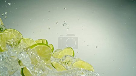 Photo for Freeze Motion of Flying Slices of Limes with Splashing Water. Isolated on Grey Background, closeup. - Royalty Free Image