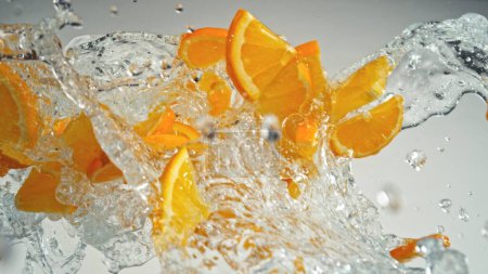 Téléchargez les photos : Congeler le mouvement des tranches volantes d'oranges avec éclaboussure d'eau. Isolé sur fond gris, gros plan. - en image libre de droit