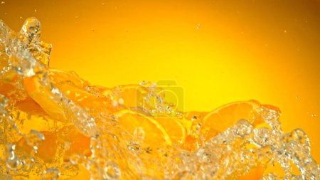 Téléchargez les photos : Congeler le mouvement des tranches volantes d'oranges avec éclaboussure d'eau. Isolé sur fond coloré, gros plan. - en image libre de droit