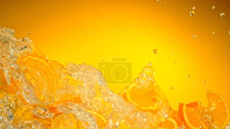 Foto de Freeze Motion of Flying Slices of Oranges with Splashing Water (en inglés). Aislado sobre fondo de color, primer plano. - Imagen libre de derechos