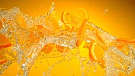 Téléchargez les photos : Congeler le mouvement des tranches volantes d'oranges avec éclaboussure d'eau. Isolé sur fond coloré, gros plan. - en image libre de droit