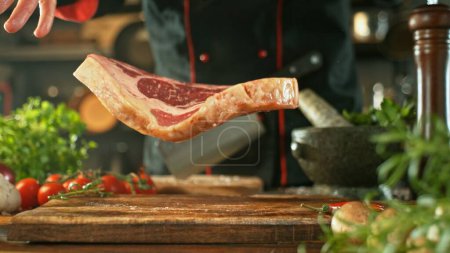 Foto de Chef lanzando carne cruda de res en tablero de corte de madera. Preparación de la carne, ingredientes alrededor. - Imagen libre de derechos