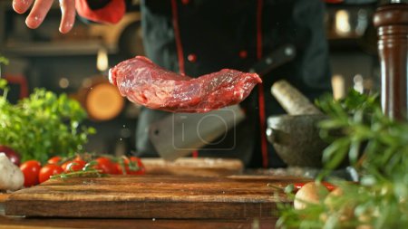 Foto de Chef lanzando carne cruda de res en tablero de corte de madera. Preparación de la carne, ingredientes alrededor. - Imagen libre de derechos
