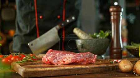 Foto de Filete de carne cruda servido en tablero de corte de madera. Carne deliciosa con verduras en el fondo. - Imagen libre de derechos
