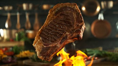 Téléchargez les photos : Savoureux steak de boeuf volant dans les airs. Cuisine avec ustensiles sur fond. Concept de nourriture volante. - en image libre de droit
