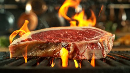 Téléchargez les photos : Steak de boeuf cru savoureux placé sur la grille de gril. Cuisine avec ustensiles sur fond. Concept de préparation des aliments. - en image libre de droit
