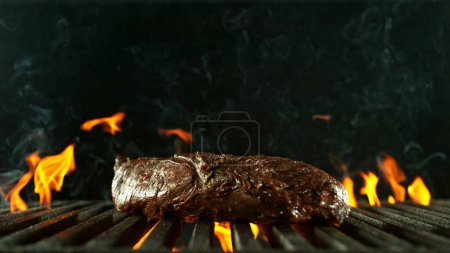 Téléchargez les photos : Steak de boeuf savoureux placé sur la grille de gril. Isolé sur fond noir. Concept de préparation des aliments. - en image libre de droit