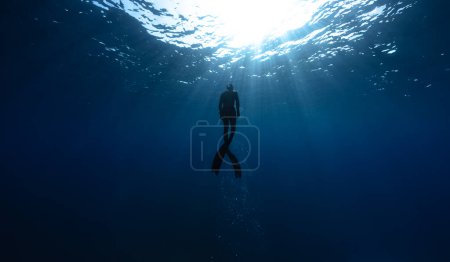 Freitaucher schwimmen in der Tiefsee mit Sonnenstrahlen. Junger Mann beschwert sich über das Leben im Meer.
