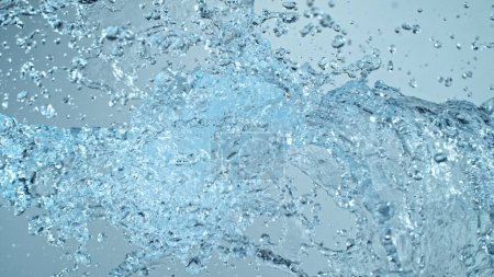 Foto de Salpicaduras de agua Volando en el aire sobre fondo azul. Congelar el movimiento de salpicaduras de agua realistas. - Imagen libre de derechos